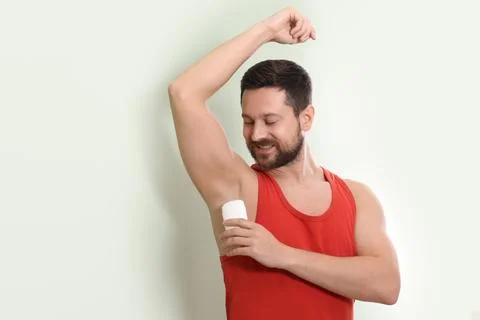 Smiling man applying solid deodorant on light green background. Space for tex 写真素材