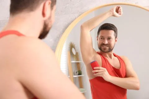 Smiling man applying solid deodorant near mirror at home Stock Photos