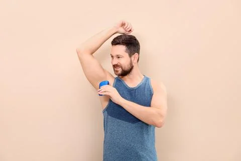 Smiling man applying solid deodorant on beige background Stock Photos