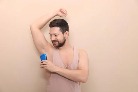 Smiling man applying solid deodorant on beige background Stock Photos
