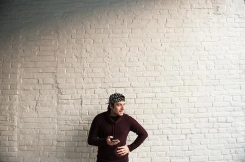 Smiling man in a baseball cap and sweater holding a smartphone in his hand Stock-Fotos