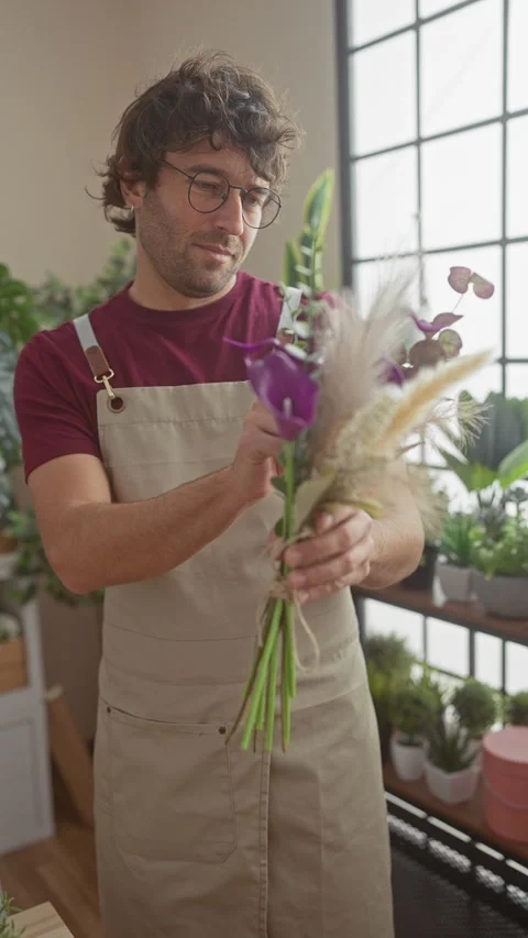 Smiling man with beard arranging a bouquet in a flower shop filled with gre.. Video stock 271083167