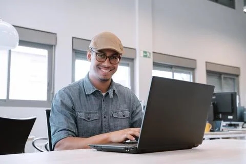 Smiling man in cap using laptop at modern office desk. Foto stock