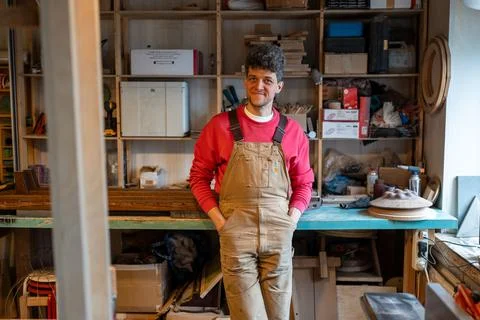 Smiling man carpenter resting in workshop looking at camera putting hands in Stock-Fotos