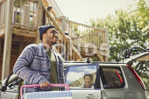 Smiling man carrying cooler outside car and sunny cabin Stock Photos
