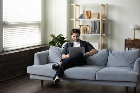 Smiling man in casual using laptop computer on comfortable couch Stock Photos