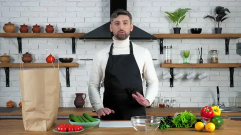 Smiling man chef in apron greets tells records online webinar in home kitchen Stock Footage 146651215