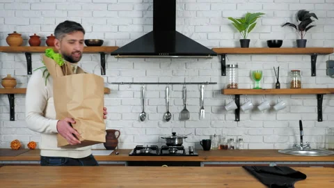 Smiling man chef comes kitchen puts paper bag with fresh food vegetable on table Stock Footage 146769156