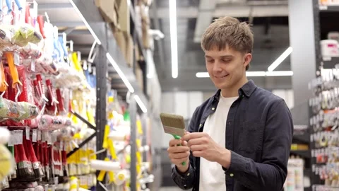 Smiling man choosing paint brush for home renovation in hardware store. Stock Footage 317083744