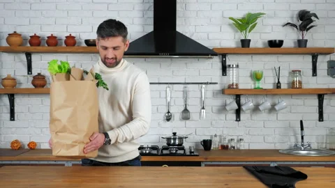 Smiling man comes to home kitchen puts paper bag with fresh vegetables on table Stock Footage 149745849
