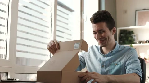 Smiling man customer opening parcel cardboard box sitting at home office Stock Footage 202278737