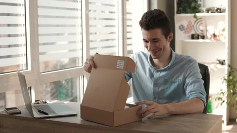 Smiling man customer opening parcel cardboard box sitting at home office desk. Stock Footage 202280142