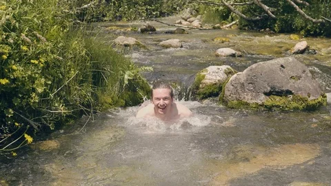 Smiling man dipping and bathing in cold river water at summer day. Slow motion Stock Footage 95142353