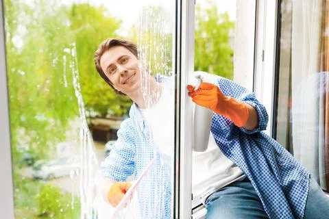 Smiling man doing spring cleaning and window washing at home. He wears oran.. Stock-Fotos