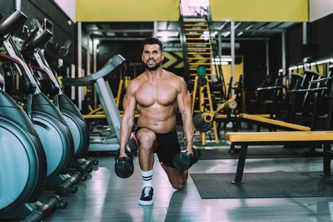 Smiling man doing squats with weights in a gym Stock Photos
