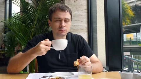 Smiling man drinking coffee and eating breakfast with fresh bakery in city cafe Stock Footage 166524269