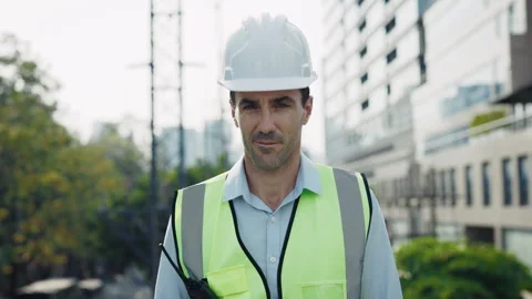 Smiling man engineer with radio set looking at camera standing at construction Stock Footage 308464432