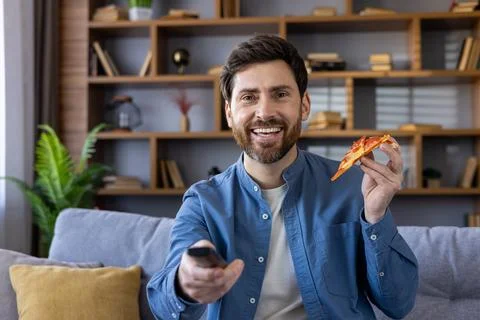 Smiling man enjoying pizza while watching TV at home Stock Photos