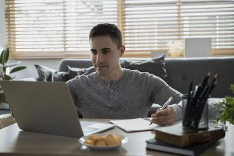 Smiling man freelancer using laptop computer and making note on notebook. 写真素材