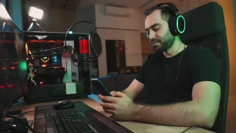 A smiling man gamer is using his smartphone while sitting near powerful computer Video stock 154451992