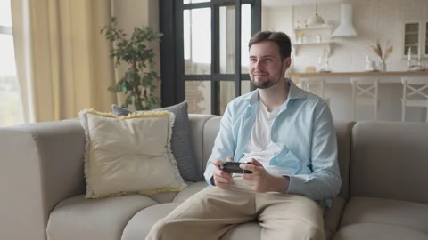 Smiling Man Gaming on Console While Lounging on Cozy Sofa at Home Very Relaxed 스톡 동영상 301246980