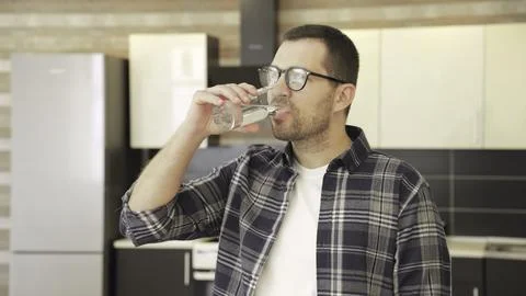 Smiling man in glasses posing at the kitchen while drinking water. Slow motion Stock Photos