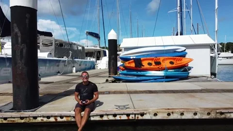 Smiling man in glasses sits on the edge of a pier in a yacht marina Stock Footage 201547418