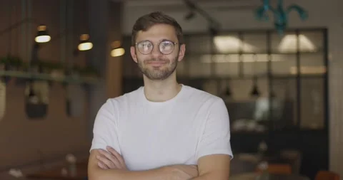 Smiling man in glasses standing in cafe indoors crossing hands in slow motion Video stock 164491209