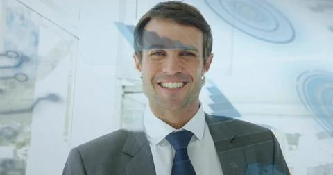 Smiling man in grey suit jacket and navy tie standing in modern office with blue Stock Photos