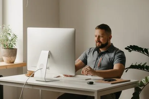 A smiling man guy with a beard is watching a video conference at home Stock Photos