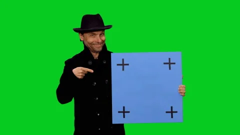 Smiling man in hat and coat looking at camera and pointing blue blank board Vídeo Stock 130795786