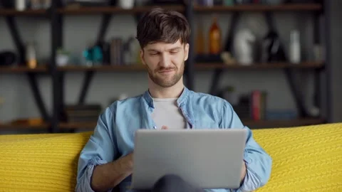 Smiling man having video call on laptop sitting on sofa Stock Footage 148962380