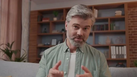 Smiling man having video call while sitting at home on sofa. Blogger doing a Vídeos de archivo 220202931