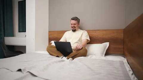 Smiling man having a video call on a laptop in a bedroom Vídeo Stock 328034448