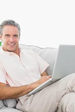 Smiling man on his couch using laptop looking at camera 스톡 사진