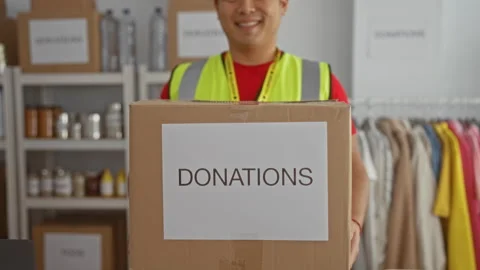 Smiling man holding donation box in charity center surrounded by organized .. Stock Footage 310064307