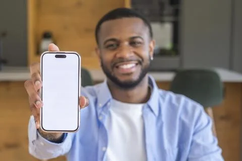 Smiling man holding smartphone to camera with blank screen, displaying an a.. 스톡 사진