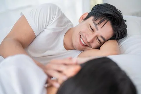 Smiling man interacts lovingly with partner in cozy bedroom during morning .. Stock Photos