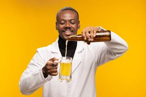 Smiling man in a lab coat pouring beer into a glass with a cheerful expression Stock Photos
