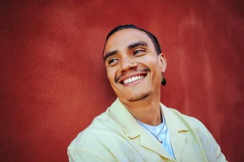 Smiling man leans by a red wall in an urban outdoor portrait Stock Photos