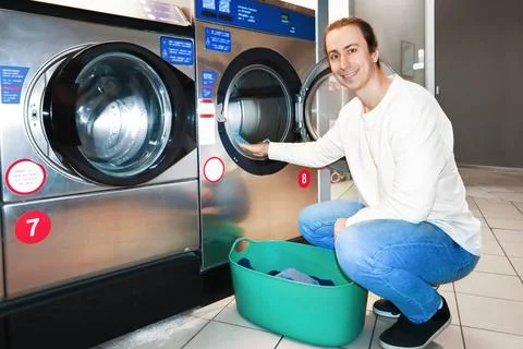 Smiling man loading clothes into a washing machine from a green basket at a.. 스톡 사진