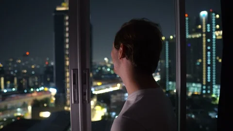 Smiling Man Looking Out Window High Above The City at Night Stock Footage 124453656