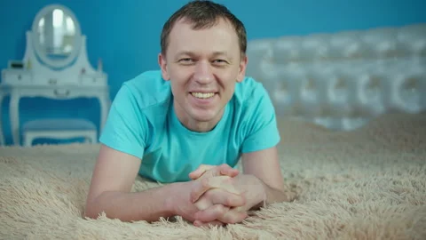 Smiling man lying on bed in bedroom and looking at camera Stock Footage 145942765