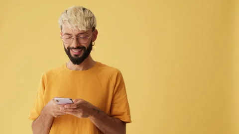 Smiling man with mobile phone in his hands shows thumbs up, isolated on yellow Stock Footage 256162816