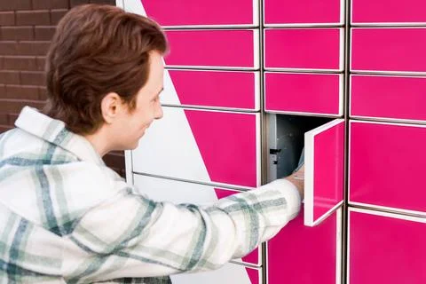 Smiling man picking up a package from an automated parcel locker. Convenien.. Stock Photos