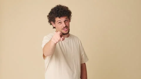 Smiling man pointing finger at camera in studio on beige background Stock Footage 252207263
