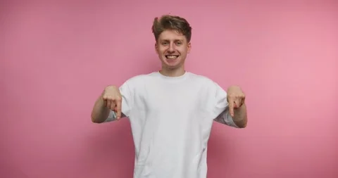 Smiling man points down in a playful manner against a pink background, show.. Stock Footage 317327969