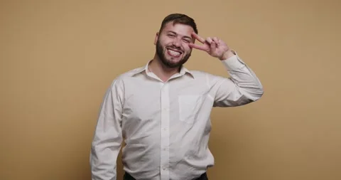 Smiling man poses playfully against a bright yellow backdrop while expressi.. Stockbeeldmateriaal 329110165