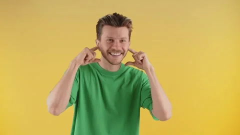 Smiling man posing for the camera with his fingers plugging his ears. A guy in Stock Footage 240471886