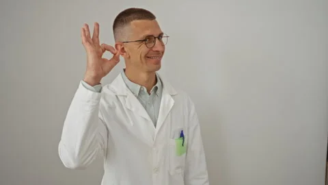 Smiling man posing with ok gesture wearing white lab coat against a white b.. Stock Footage 289261456